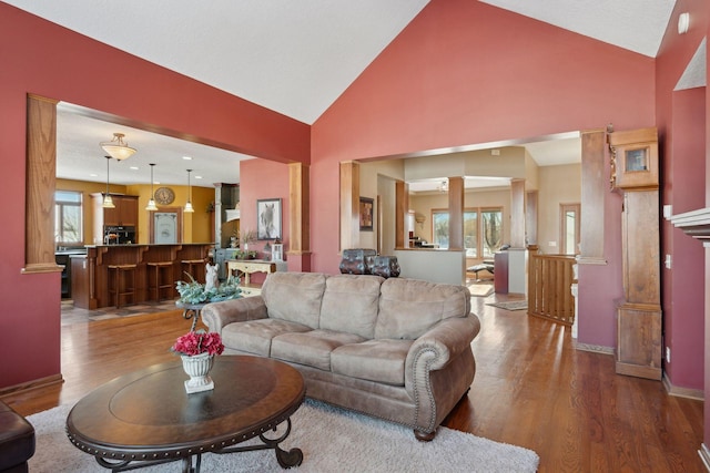 living area featuring ornate columns, baseboards, high vaulted ceiling, and wood finished floors