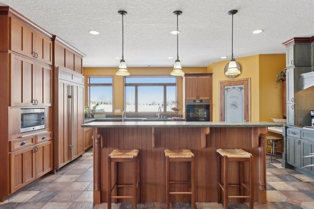 kitchen with black oven, brown cabinets, stainless steel microwave, a kitchen bar, and pendant lighting