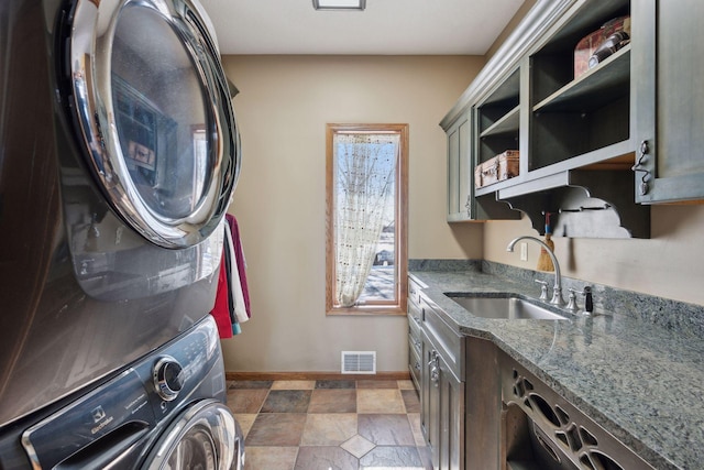 laundry area with cabinet space, visible vents, stacked washer / dryer, stone finish floor, and a sink