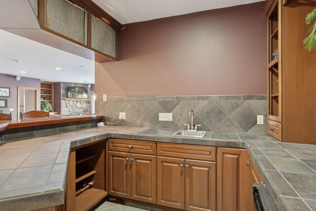 kitchen with tile countertops, open shelves, brown cabinetry, and a sink