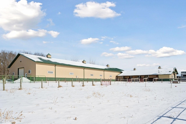 snow covered property featuring a garage, an outbuilding, a pole building, and fence