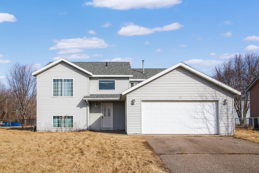 traditional-style home featuring fence, roof with shingles, concrete driveway, a front yard, and a garage