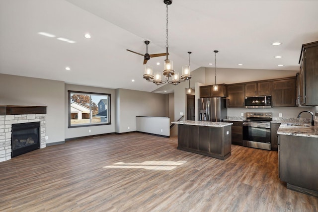 kitchen featuring light stone counters, hanging light fixtures, appliances with stainless steel finishes, a kitchen island, and a fireplace