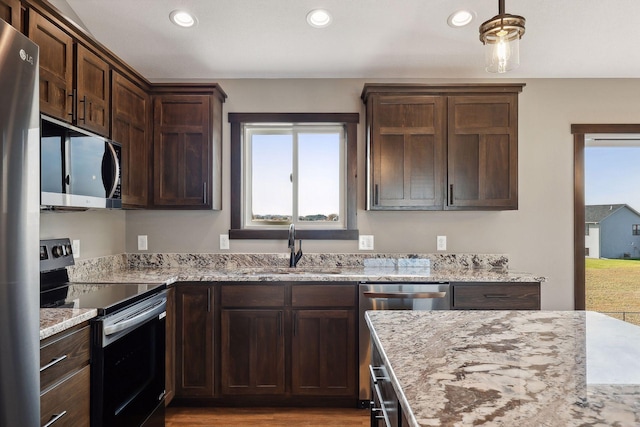 kitchen with dark brown cabinetry, sink, light wood-type flooring, stainless steel appliances, and light stone countertops