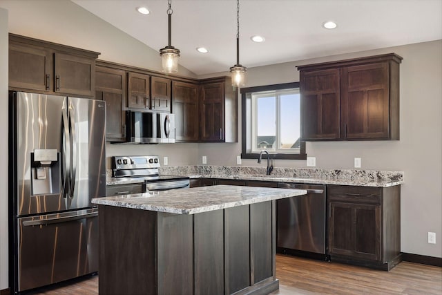 kitchen with appliances with stainless steel finishes, hanging light fixtures, wood-type flooring, a kitchen island, and vaulted ceiling