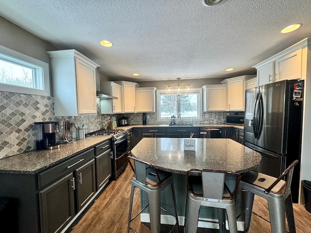 kitchen with a kitchen island, wood-type flooring, appliances with stainless steel finishes, and dark stone counters