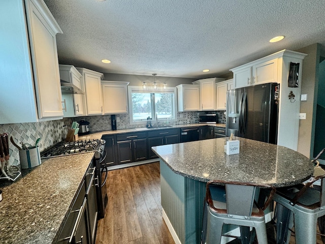 kitchen featuring white cabinetry, dark stone counters, a center island, and black appliances