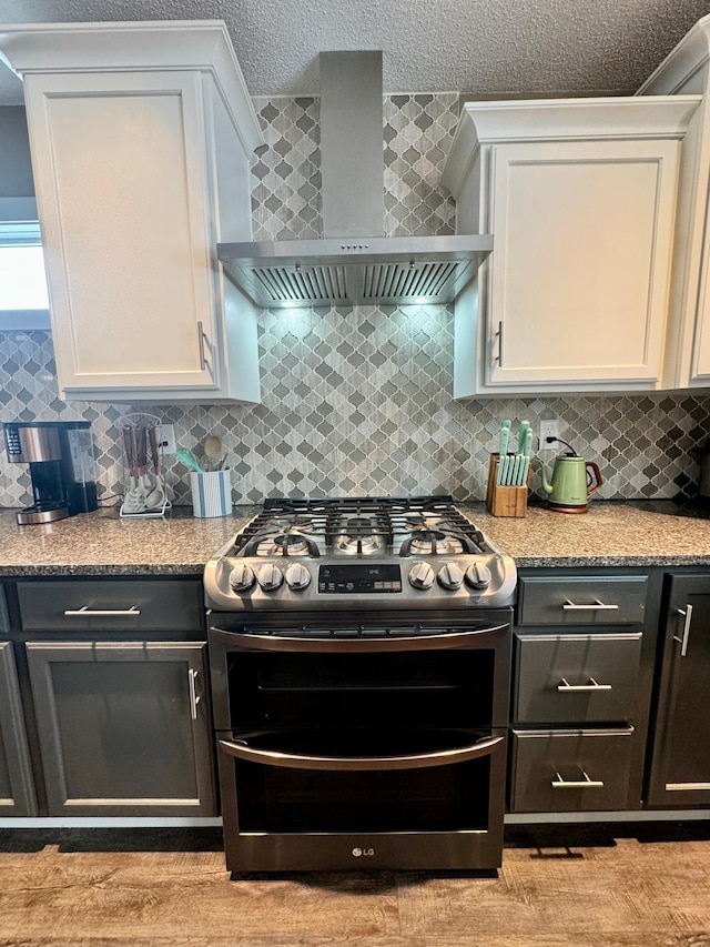 kitchen featuring double oven range, wall chimney range hood, white cabinets, and decorative backsplash