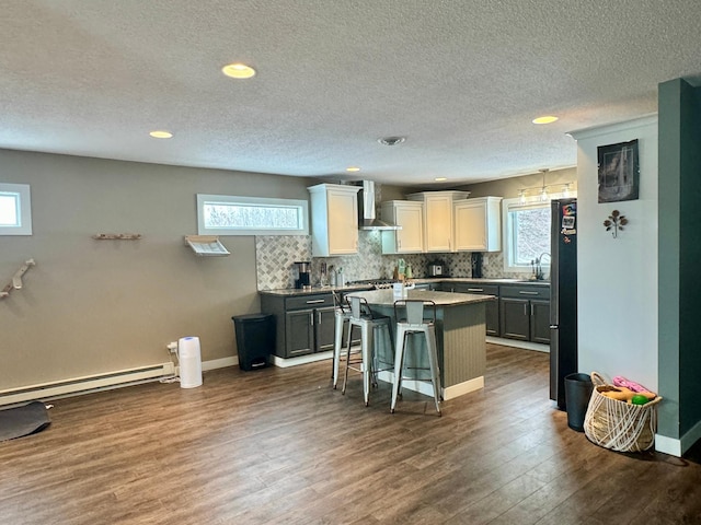 kitchen featuring wall chimney exhaust hood, a breakfast bar, white cabinetry, fridge, and a kitchen island