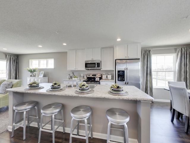 kitchen with white cabinetry, stainless steel appliances, an island with sink, and a breakfast bar area