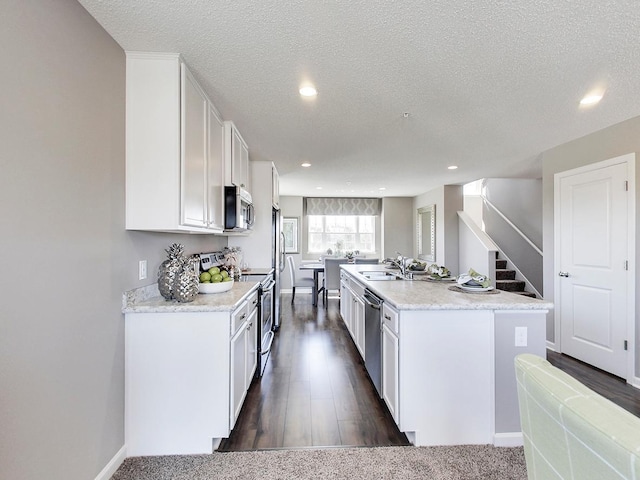 kitchen featuring white cabinetry, stainless steel appliances, dark colored carpet, an island with sink, and a textured ceiling