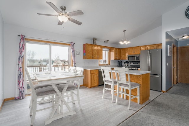 kitchen with lofted ceiling, appliances with stainless steel finishes, hanging light fixtures, a center island, and ceiling fan with notable chandelier