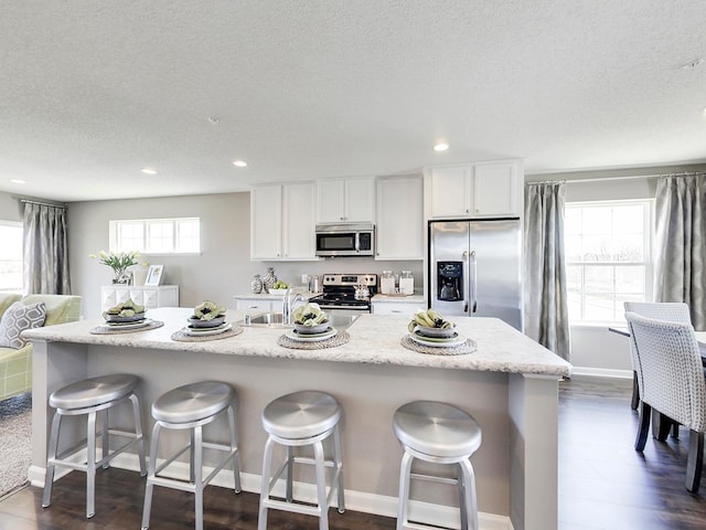 kitchen with a center island with sink, stainless steel appliances, a kitchen breakfast bar, a healthy amount of sunlight, and white cabinets