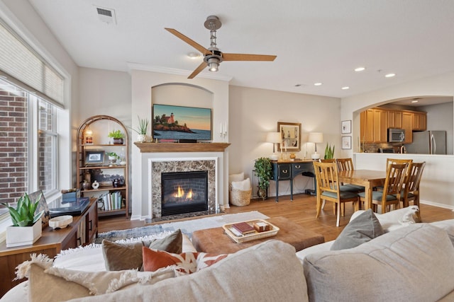 living room featuring ceiling fan, a premium fireplace, and light wood-type flooring