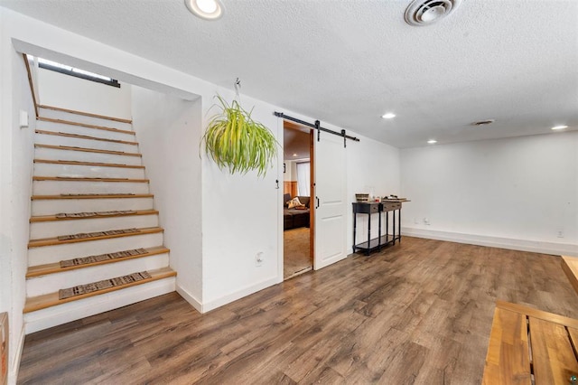 basement featuring dark wood-type flooring, a barn door, and a textured ceiling