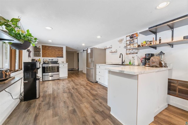 kitchen with a barn door, white cabinetry, appliances with stainless steel finishes, and hardwood / wood-style flooring