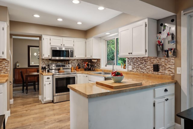 kitchen with appliances with stainless steel finishes, sink, white cabinets, and kitchen peninsula