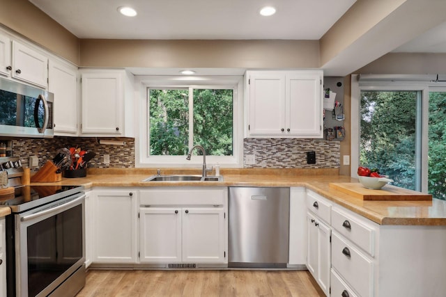 kitchen featuring appliances with stainless steel finishes, sink, white cabinets, backsplash, and light hardwood / wood-style flooring