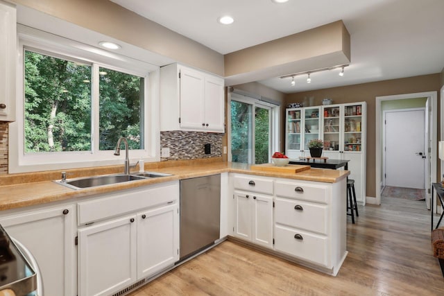 kitchen with sink, dishwasher, kitchen peninsula, decorative backsplash, and white cabinets