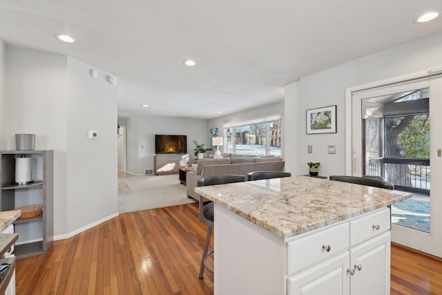 kitchen featuring light hardwood / wood-style flooring, light stone countertops, white cabinets, and a kitchen island