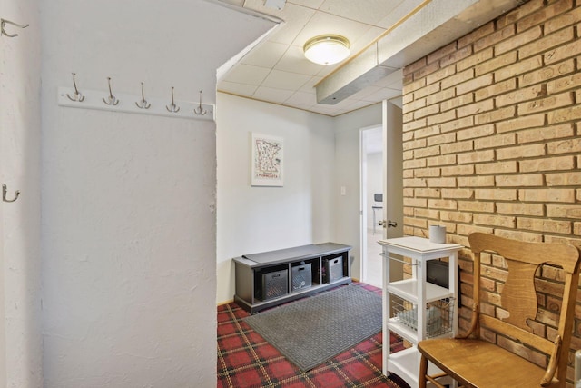 mudroom featuring a paneled ceiling and brick wall