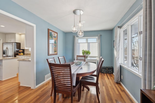 dining room with light wood-type flooring, visible vents, and baseboards