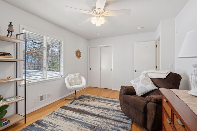 living area with baseboards, wood finished floors, visible vents, and ceiling fan