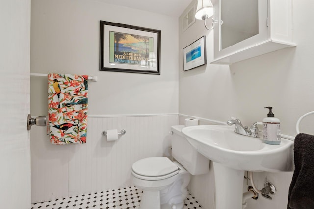 bathroom featuring toilet, visible vents, and a wainscoted wall