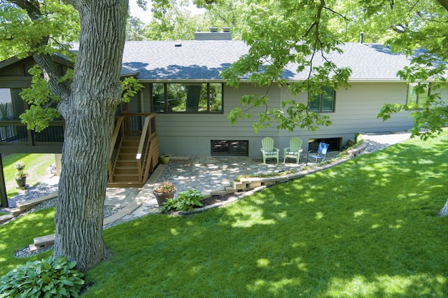 back of property featuring a patio area, a lawn, roof with shingles, and a chimney