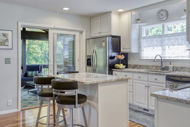 kitchen with a sink, stainless steel refrigerator with ice dispenser, white cabinetry, light wood-type flooring, and a center island