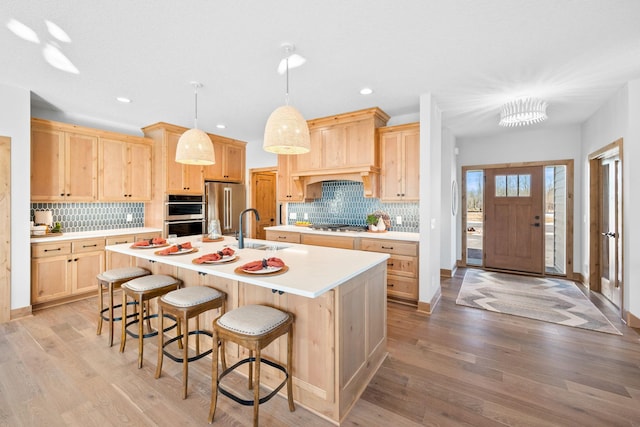 kitchen featuring appliances with stainless steel finishes, sink, hanging light fixtures, a kitchen island with sink, and light brown cabinets