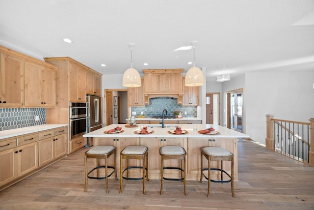 kitchen featuring pendant lighting, an island with sink, stainless steel appliances, light brown cabinets, and light wood-type flooring