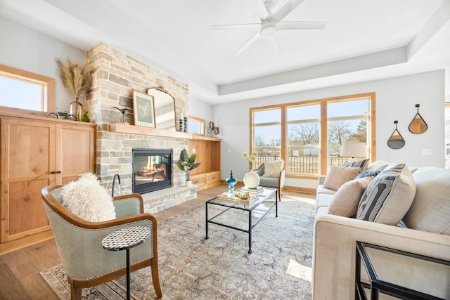 living room with a fireplace, light hardwood / wood-style flooring, a raised ceiling, and a healthy amount of sunlight