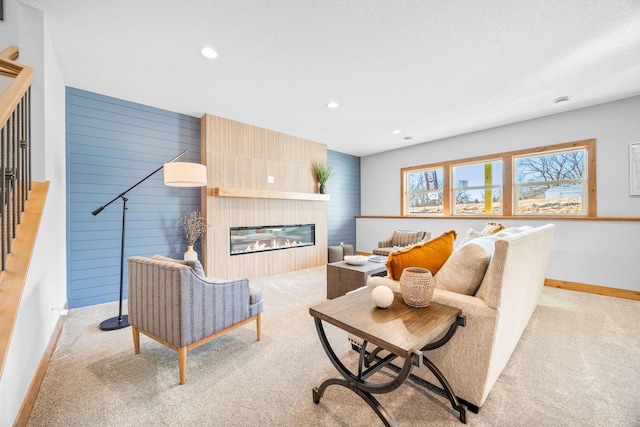 carpeted living room with wooden walls, a large fireplace, and a textured ceiling