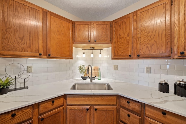 kitchen with light stone counters, sink, a textured ceiling, and backsplash