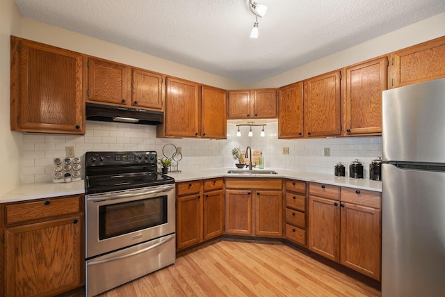 kitchen with sink, appliances with stainless steel finishes, backsplash, light hardwood / wood-style floors, and a textured ceiling