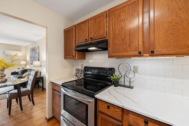 kitchen with stainless steel electric range, light stone counters, tasteful backsplash, a textured ceiling, and light wood-type flooring