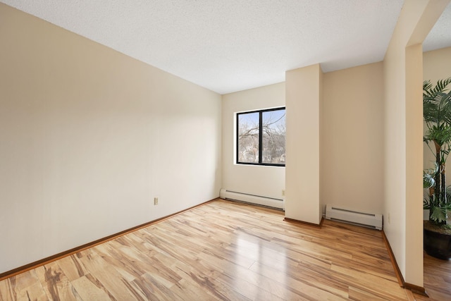 spare room featuring a baseboard heating unit, light hardwood / wood-style floors, and a textured ceiling