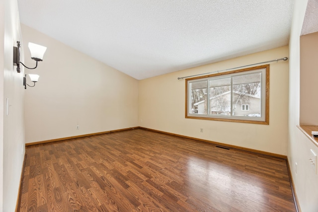 unfurnished room featuring dark wood-style floors, visible vents, vaulted ceiling, a textured ceiling, and baseboards