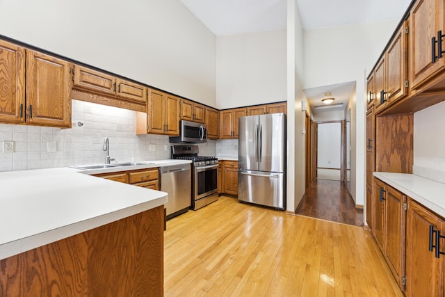 kitchen featuring a sink, light countertops, appliances with stainless steel finishes, light wood-type flooring, and brown cabinetry