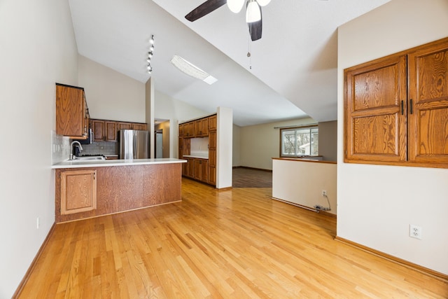 kitchen with brown cabinetry, freestanding refrigerator, a peninsula, light countertops, and a sink