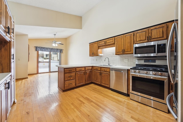 kitchen featuring brown cabinets, stainless steel appliances, light countertops, a sink, and a peninsula