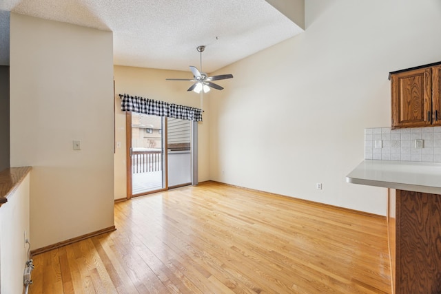 unfurnished living room featuring a ceiling fan, baseboards, a textured ceiling, and light wood finished floors