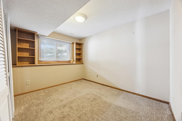 spare room with light carpet, baseboards, and a textured ceiling