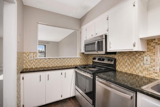 kitchen with white cabinetry, backsplash, stainless steel appliances, and dark stone counters