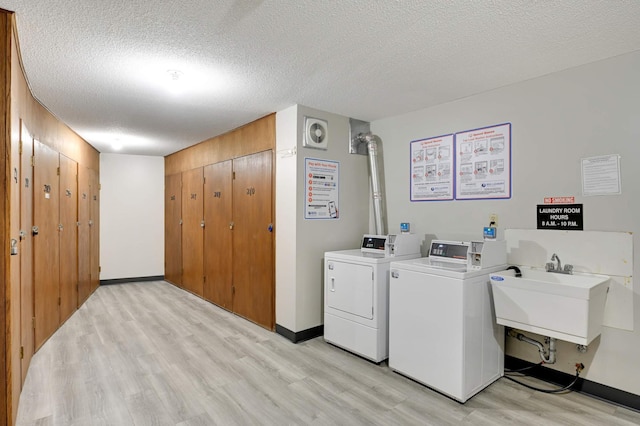 laundry area with sink, a textured ceiling, light hardwood / wood-style flooring, and washing machine and clothes dryer