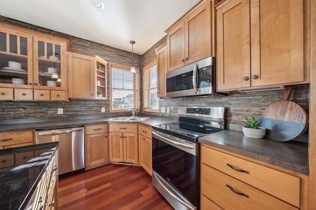 kitchen with dark countertops, glass insert cabinets, hanging light fixtures, stainless steel appliances, and a sink