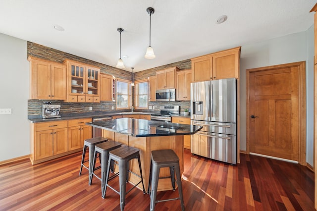 kitchen featuring dark countertops, glass insert cabinets, appliances with stainless steel finishes, a breakfast bar area, and a center island