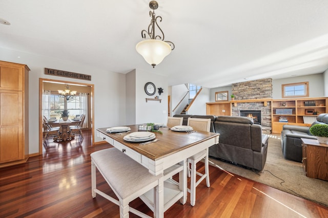 dining space with dark wood-style floors, a fireplace, stairs, and a notable chandelier