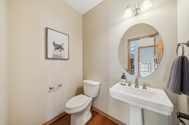 half bathroom featuring toilet, a sink, baseboards, and wood finished floors